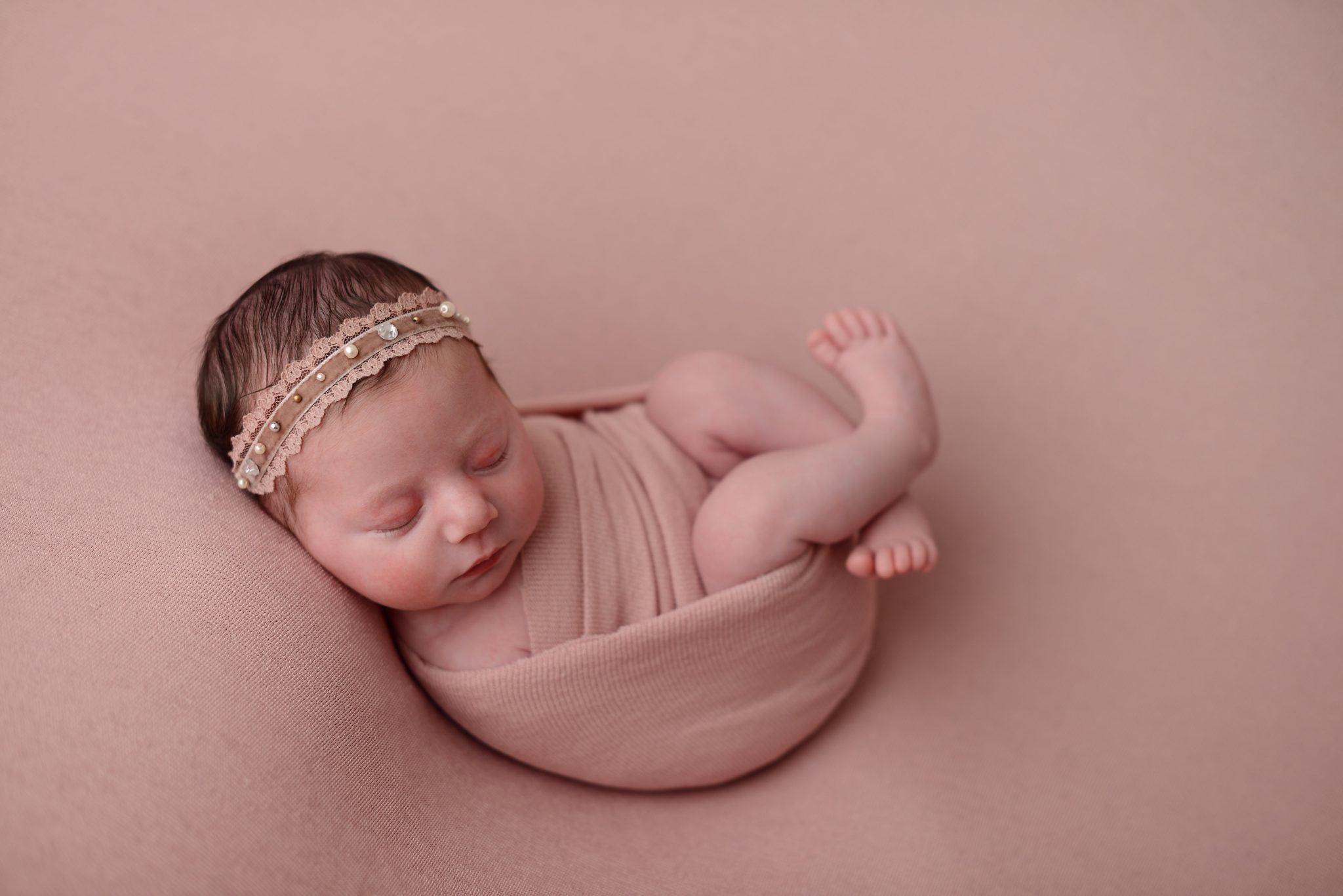 Newborn baby girl on pink background in Queens Portrait Studio